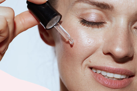 a smiling women applying retinol serum using a dropper to her face