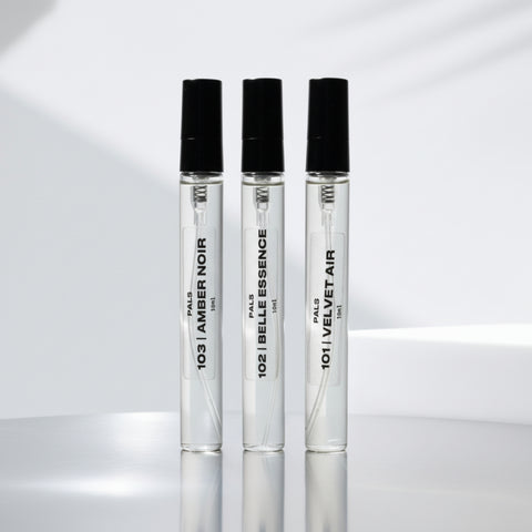 Three perfume bottles with black caps on a reflective surface with a light gray background